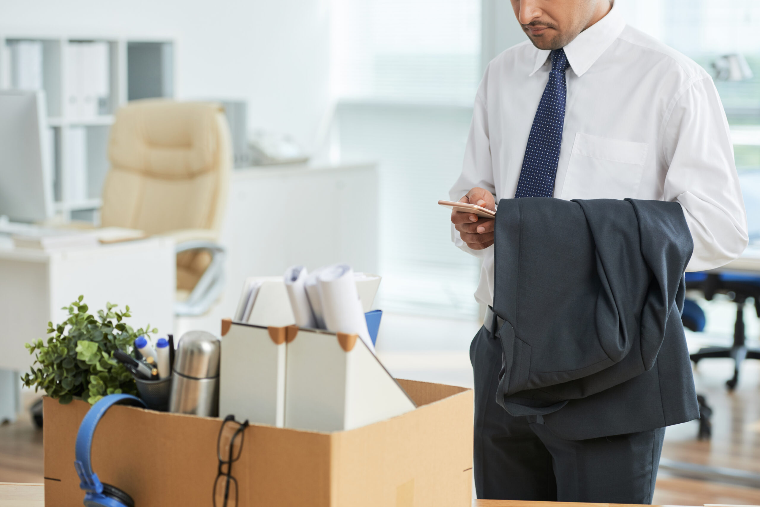 A person holds their suit jacket and phone after being laid off.